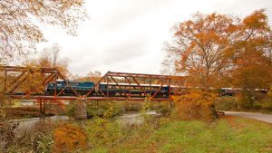 Train crossing bridge with fall colored trees in the background